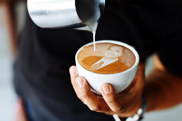 A barista pouring milk into a cappuccino featuring Raymond Conners' portrait in latte art