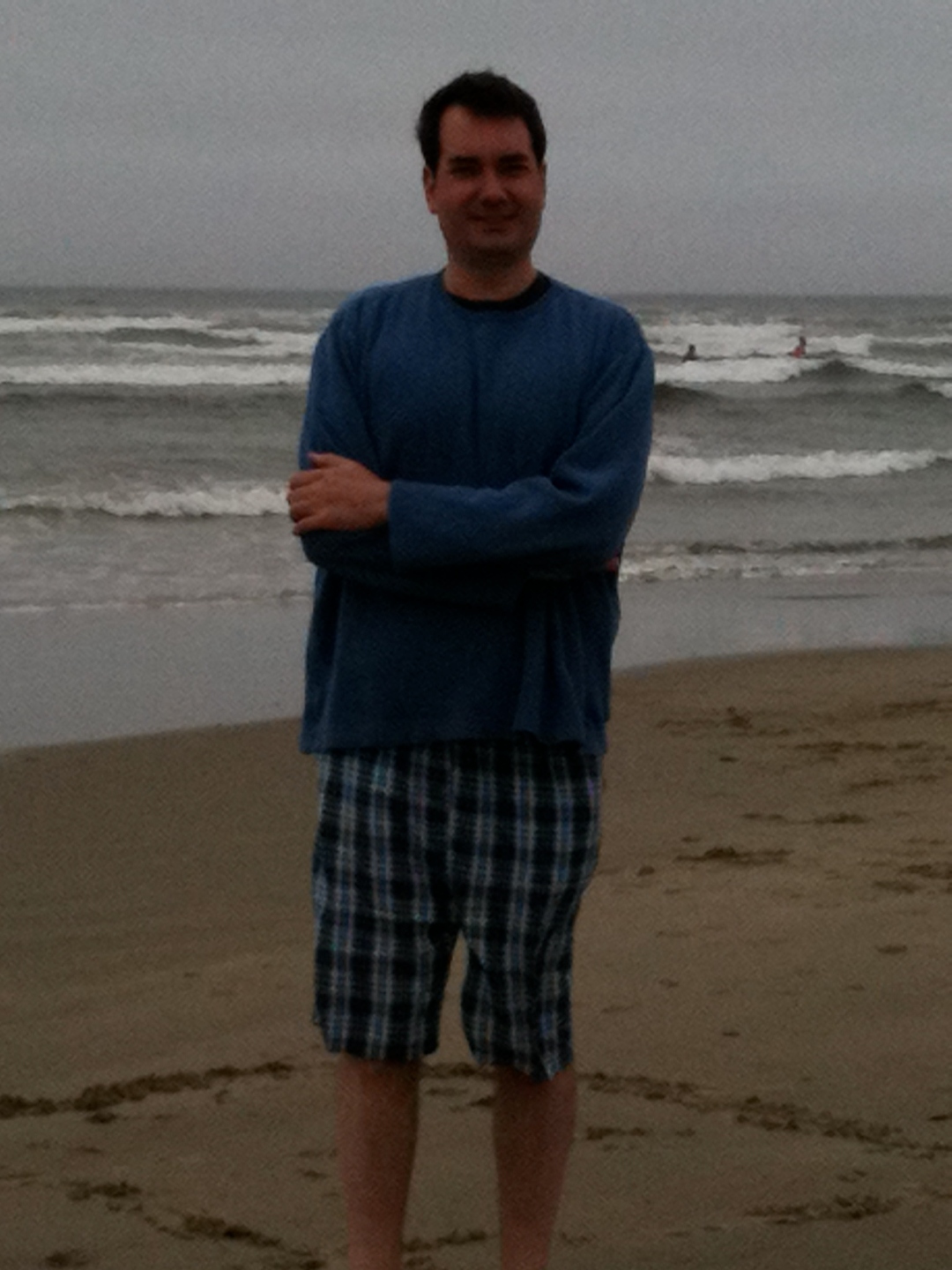 Younger Raymond on a Pacific beach at dusk, surfers in the waves behind him.