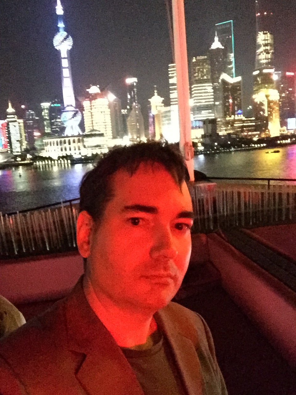Raymond on a riverboat on the Huangpu River at night with the Shanghai Pudong skyline and Oriental Pearl Tower in the background.